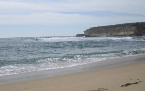 shot from the beach of a distant wave peelng right, away from a bluff