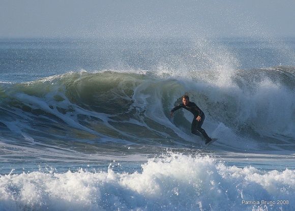 A guy in a wetsuit surfing a big, cold-looking wave in the afternoon. Photo credit: Patty Bruno.